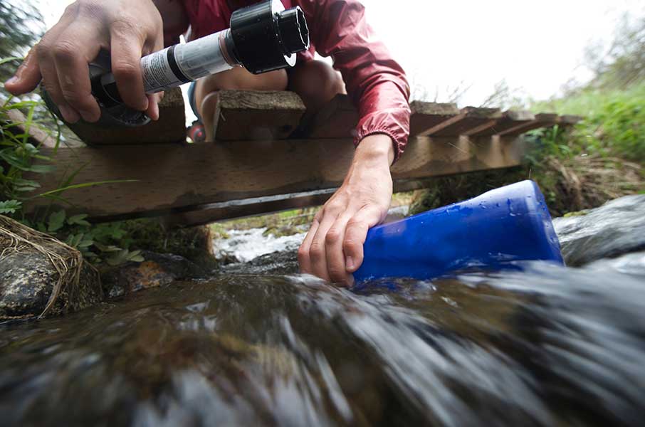 Un randonneur remplit, au milieu du courant, sa bouteille d’eau avec un filtre afin de rendre l’eau potable. Crédit : hemis.fr 